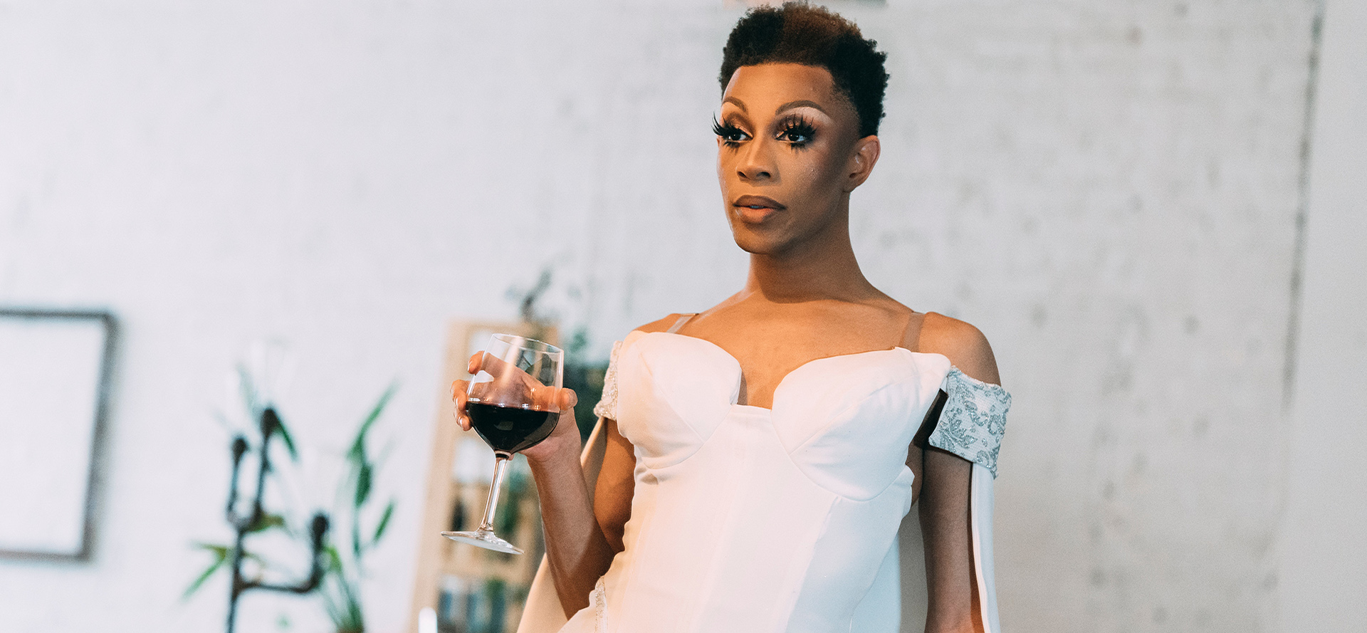 Un transsexuel en robe blanche avec un verre de vin.