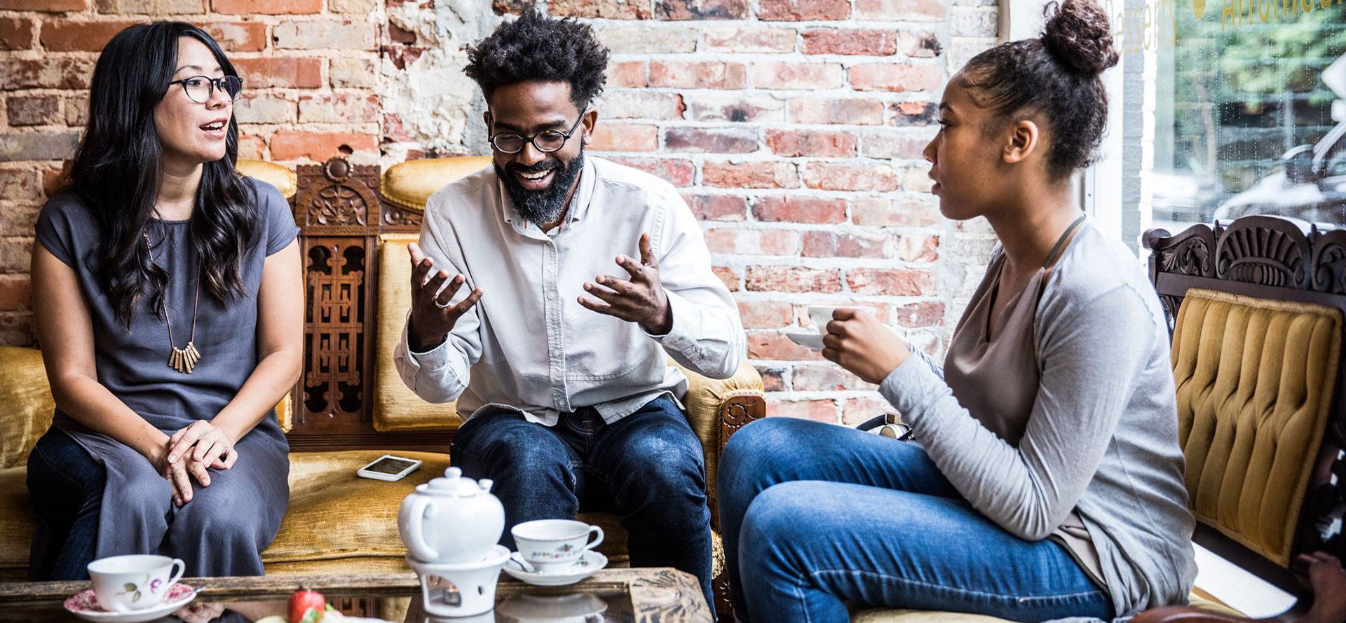 A guy and two girls talking over a cup of tea.