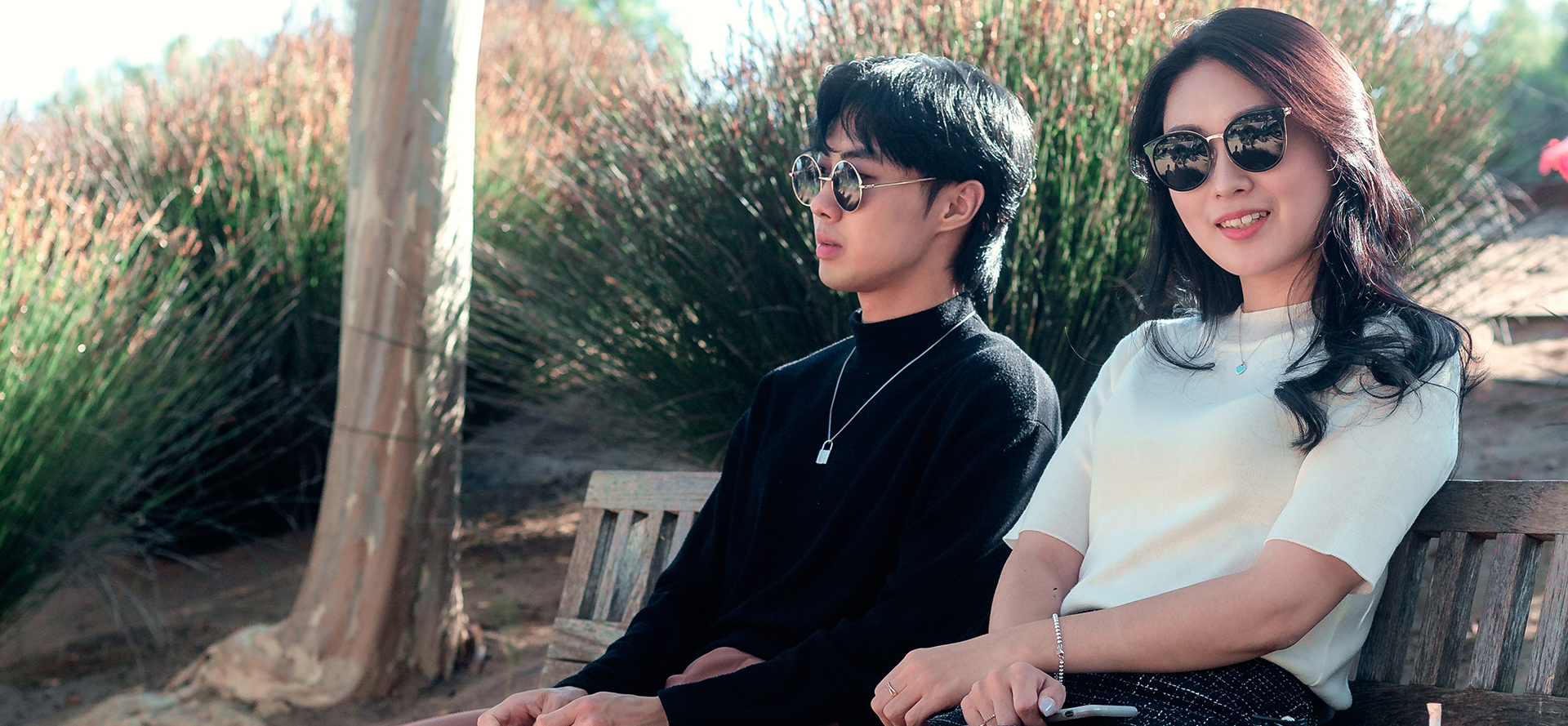 Et asiatisk par med briller sidder på en bænk.