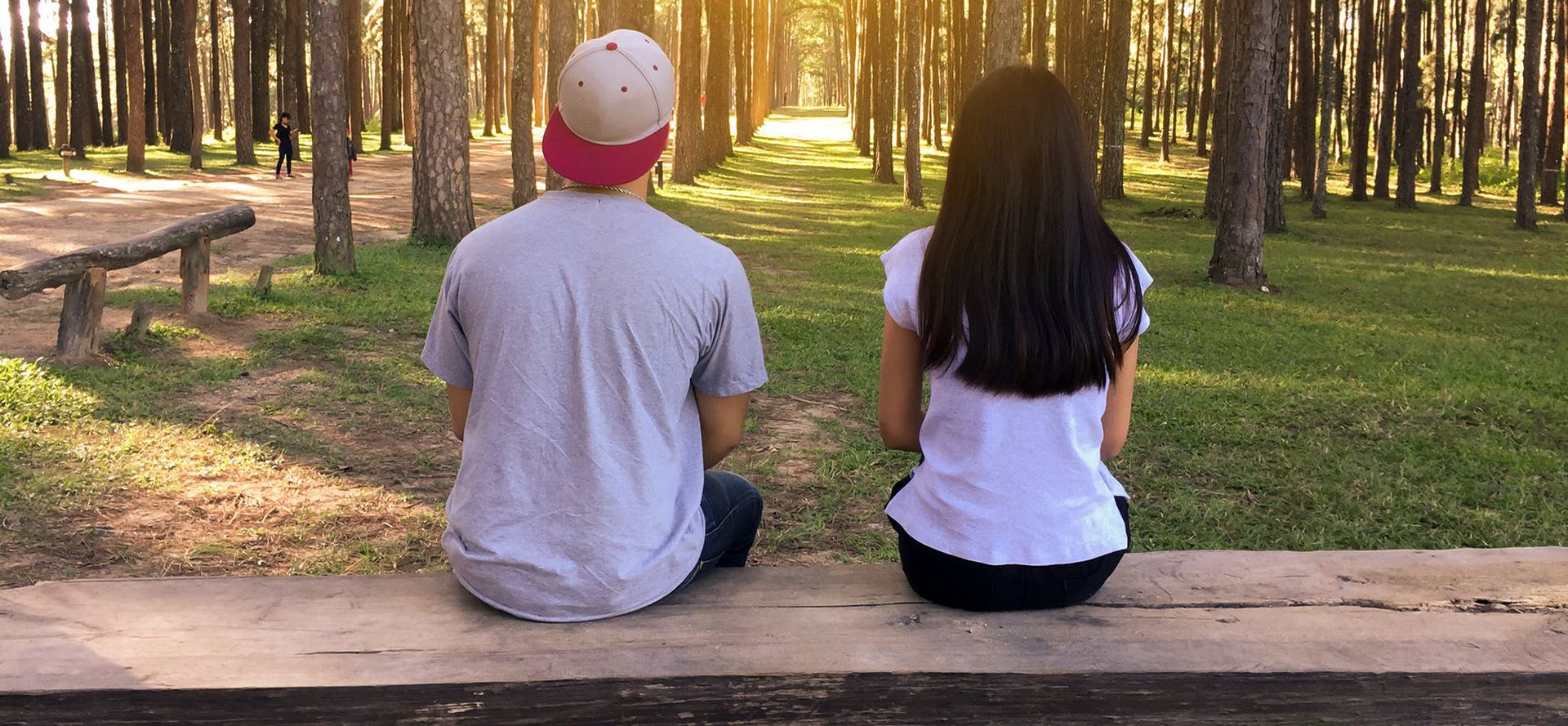A couple on their first date is sitting on a bench in the woods.