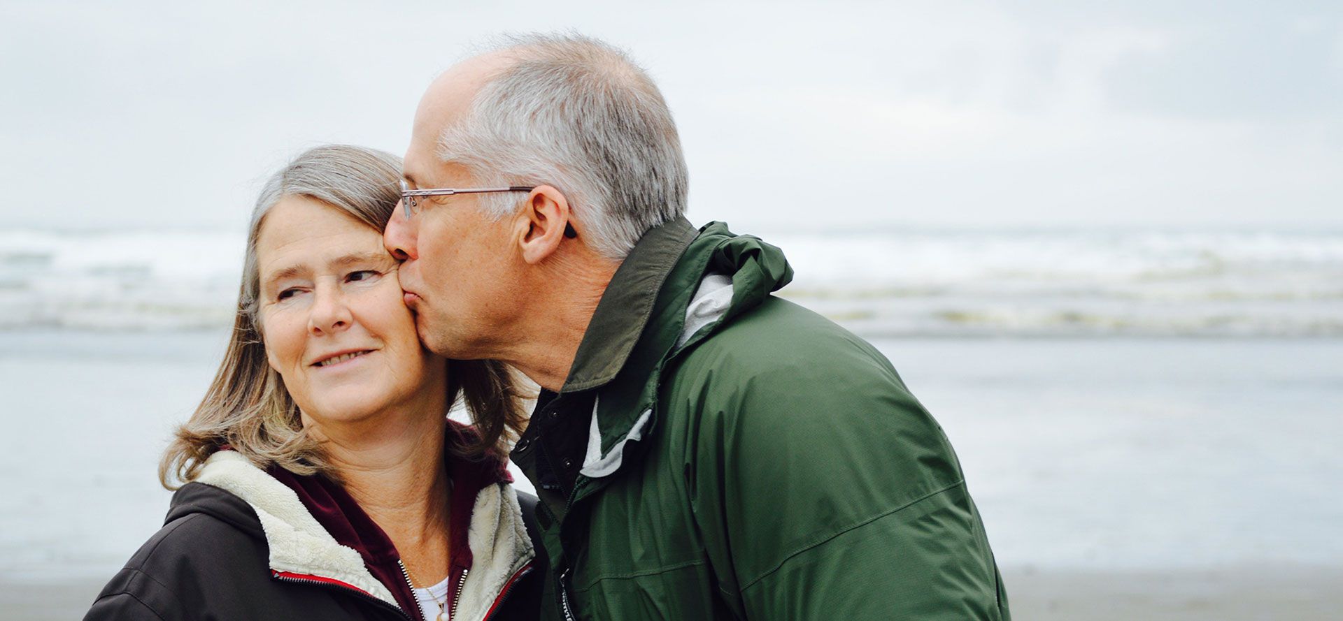 An elderly man kisses his soul mate against the background of the sea.