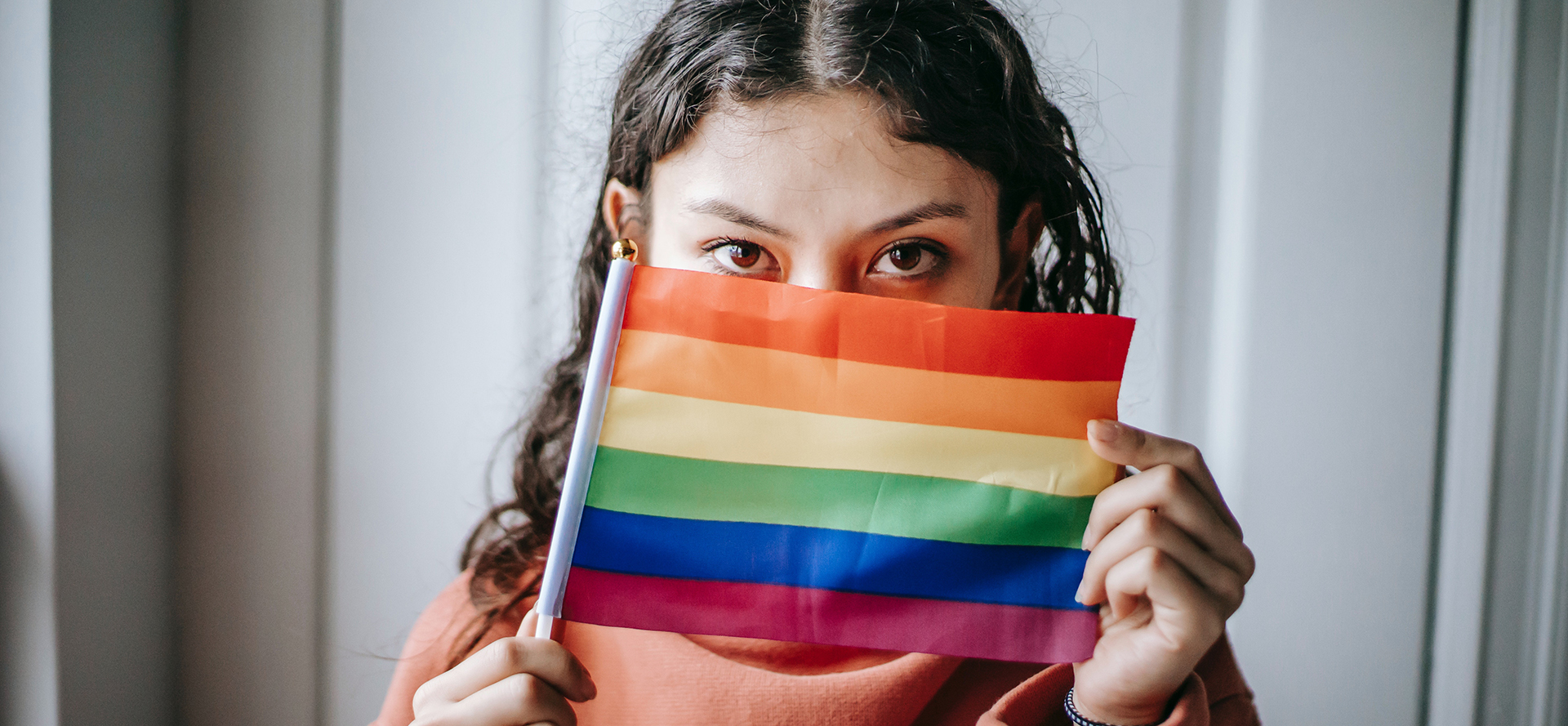 Bisexuální dívka si zakrývá obličej vlajkou LGBT.