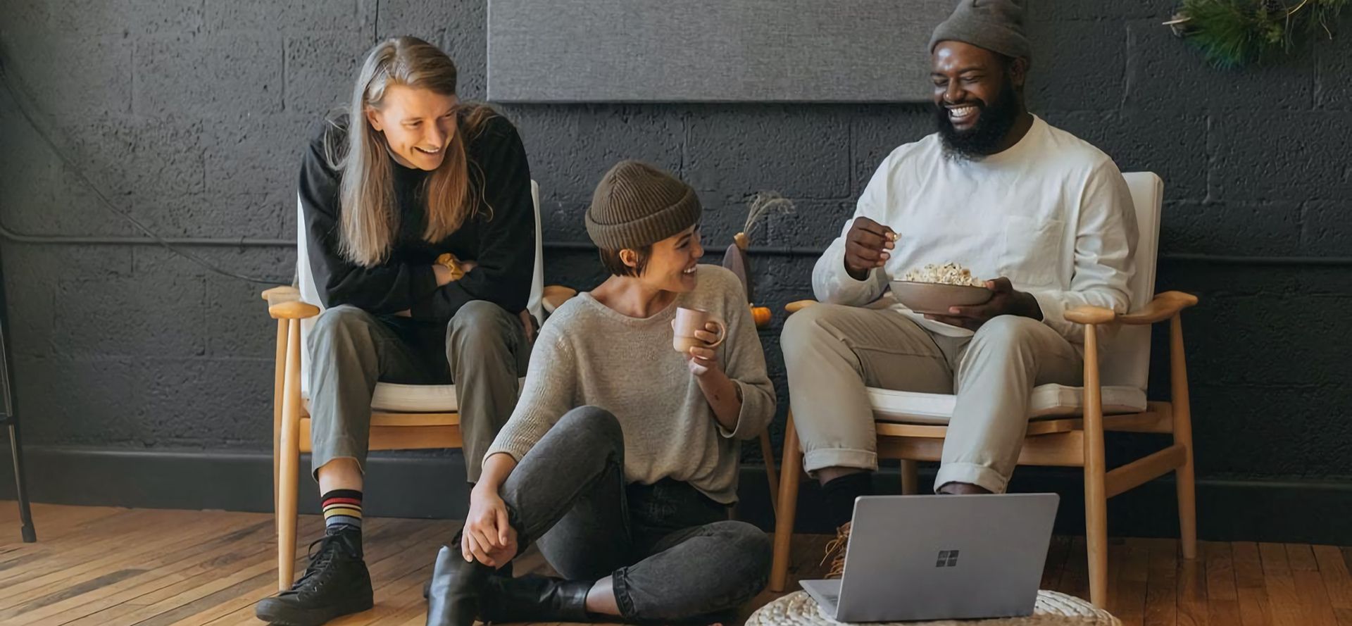 Two men and a woman watching a video on a laptop and laughing.