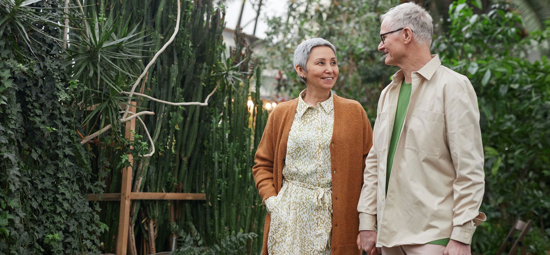 Widowed singles on a date in a greenhouse, walking and holding hands.