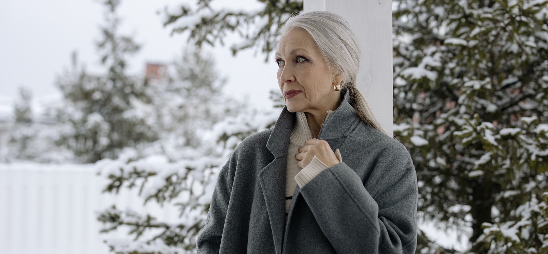 Grandma in a gray coat in front of the winter scenery.