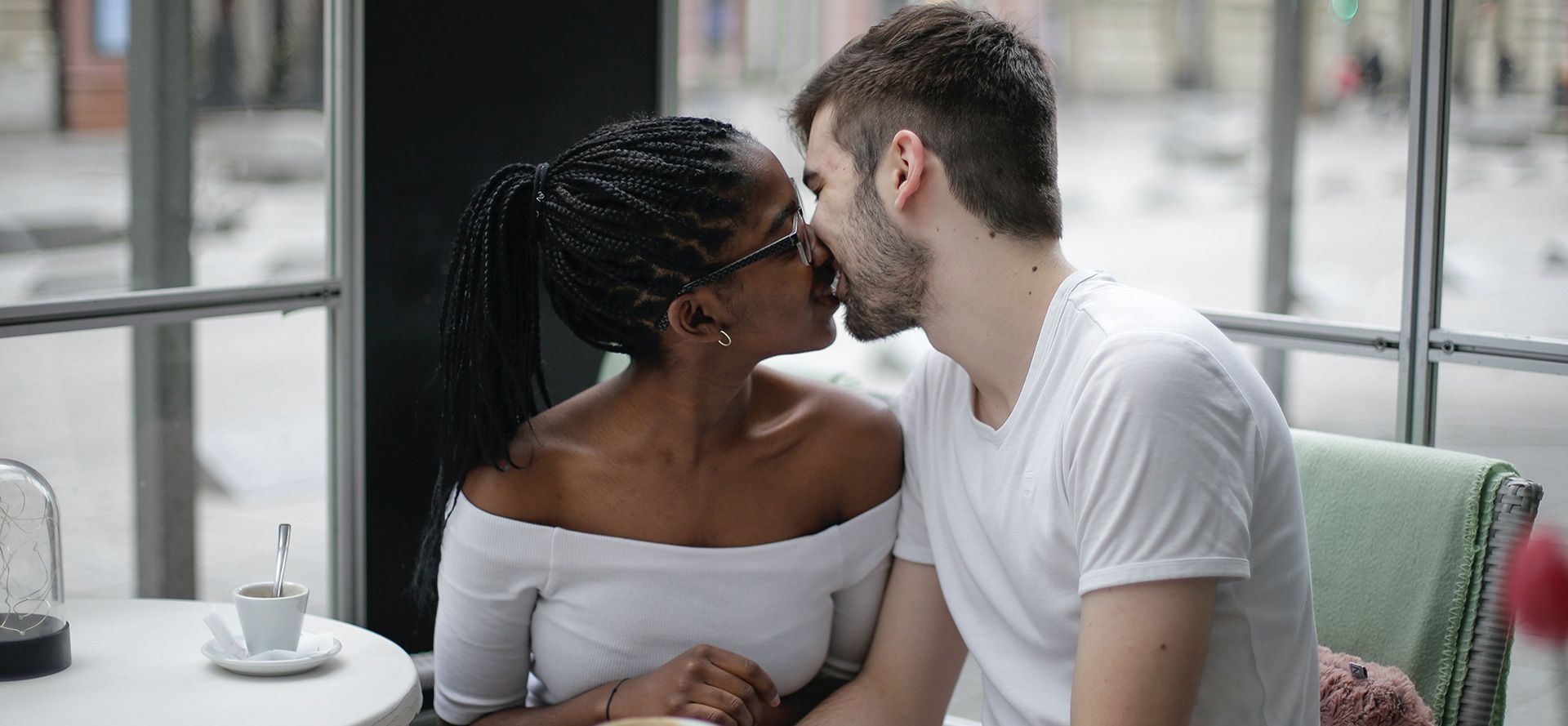 Et internationalt par kysser hinanden på en café.