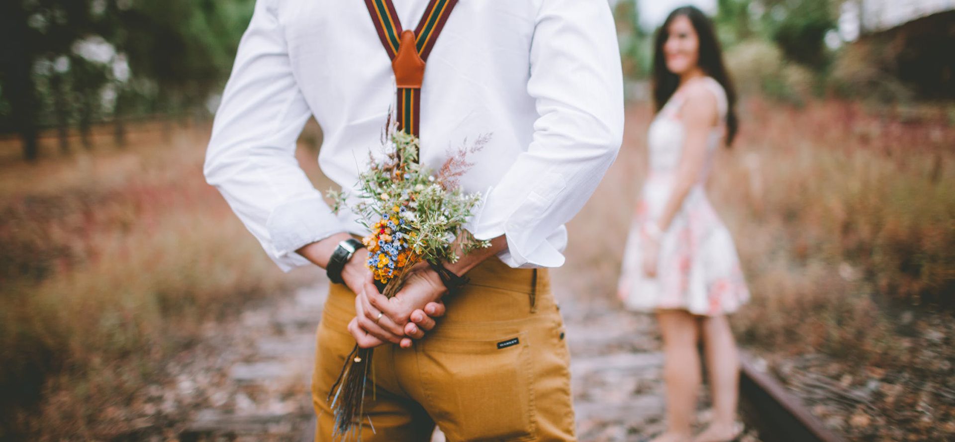 A man in a white shirt is holding a bouquet of flowers behind his back.