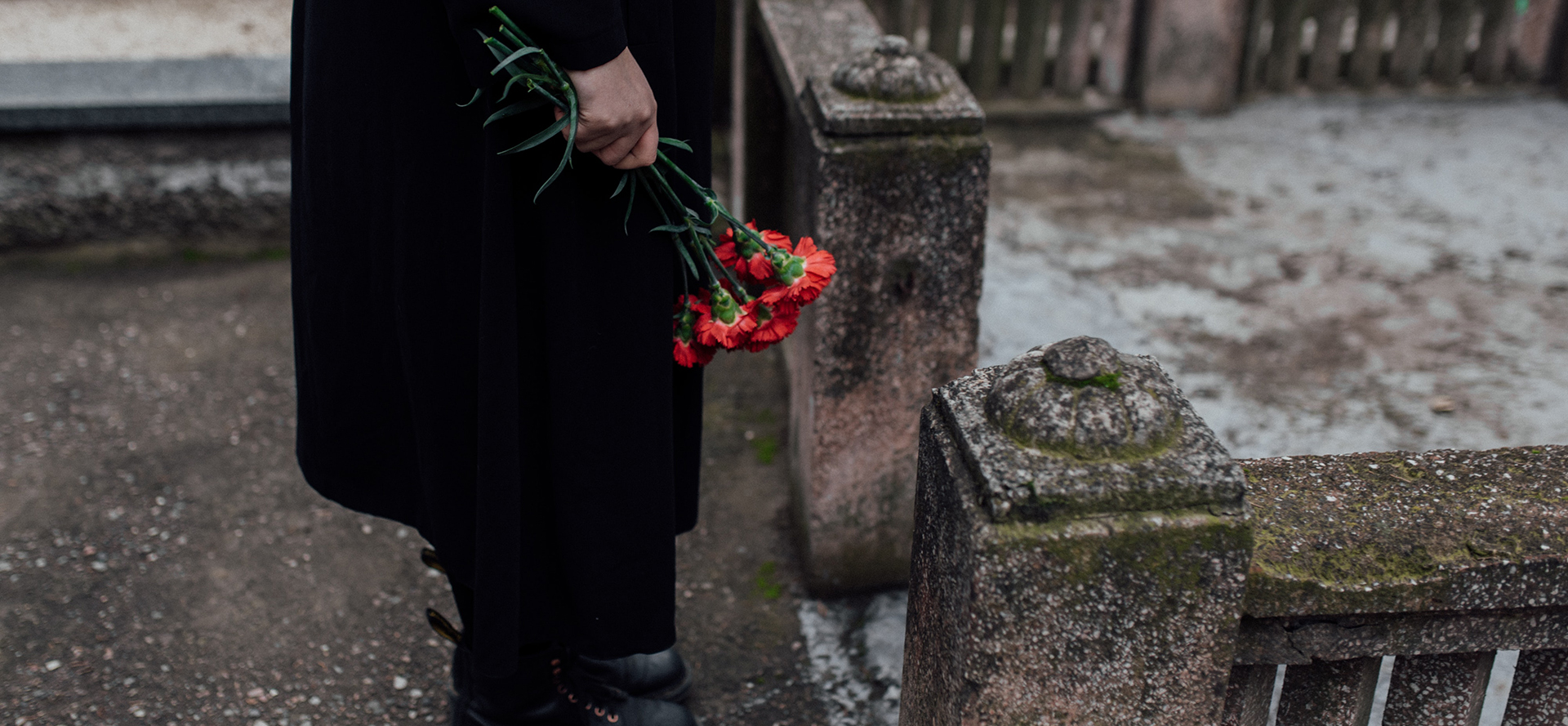 Widower in a cemetery holding flowers.